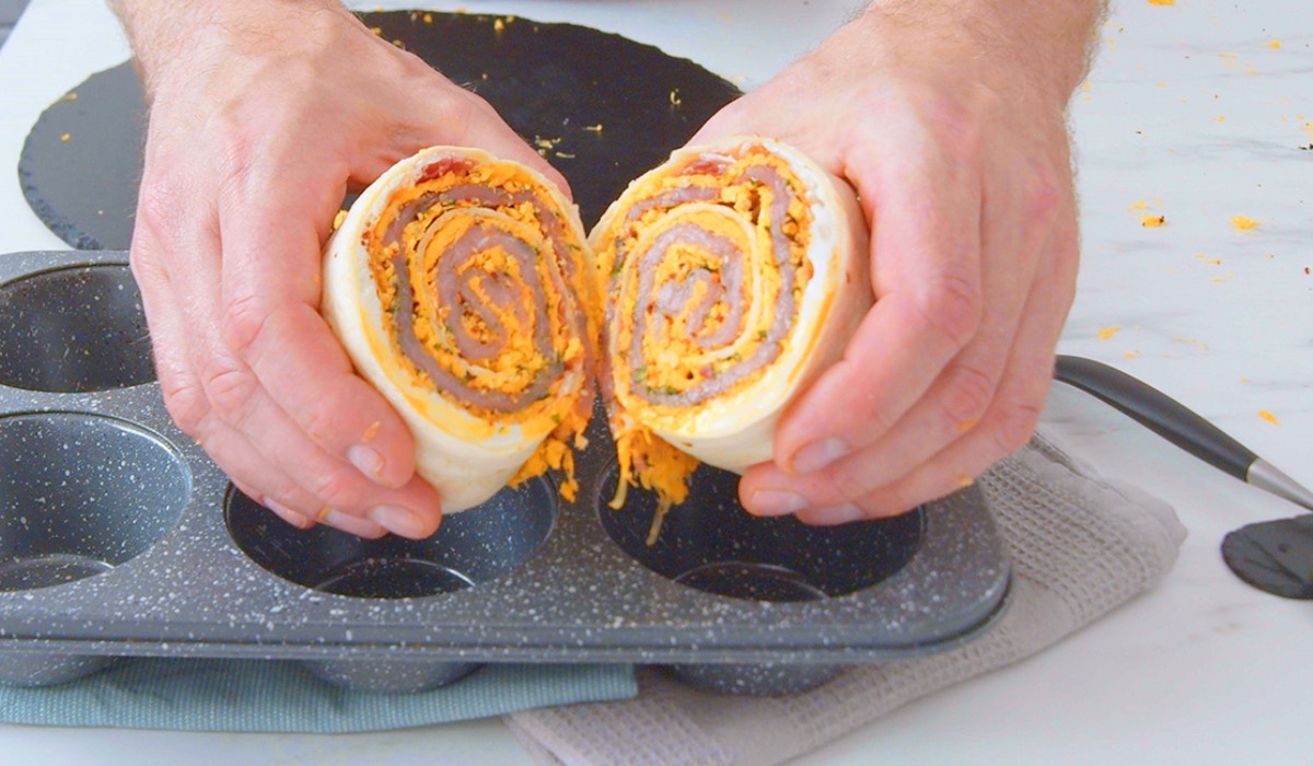 Zwei mit Käseschnitzel gefüllte Wraps werden über einer Muffinform von zwei Händen gehalten.