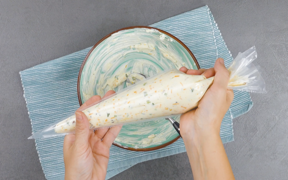 Frischkäse in Spritzbeutel wird über Schüssel gehalten