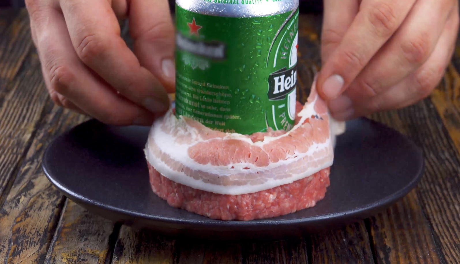 Eine Bierdose wird in eine Kugel Hackfleisch gedrückt und eine Scheibe Bacon um die Fleischmasse gelegt