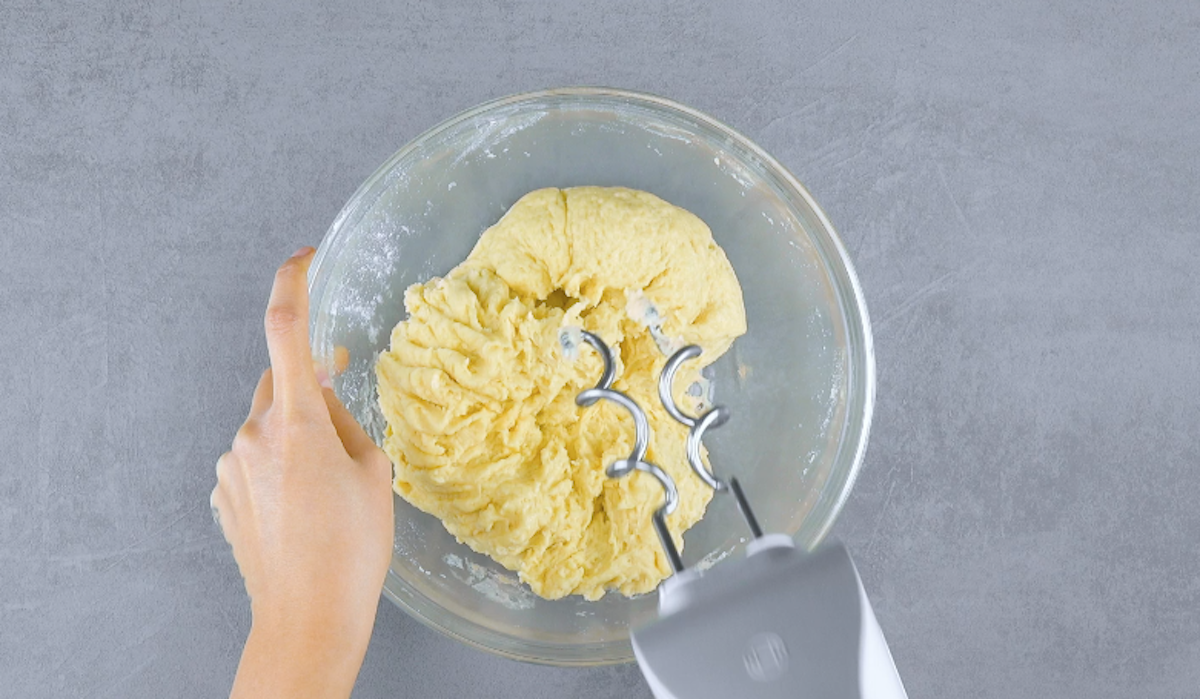 Brötchenteig wird mit Handrührgerät in Schüssel geknetet