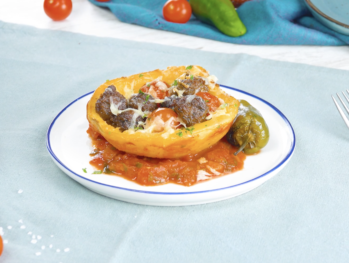 Eine halbe Kartoffel mit Fleischbällchen und Bratpaprika auf Tomatensoße