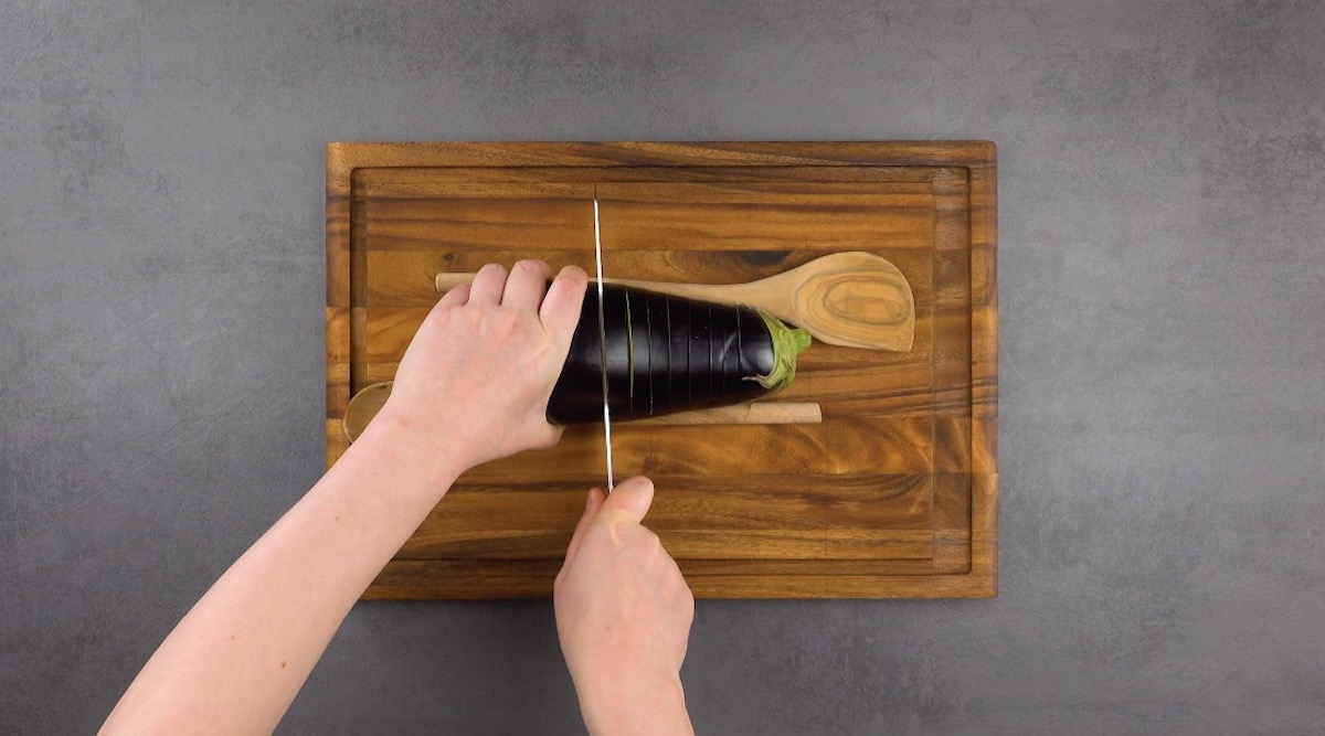 Eine Aubergine wird zwischen zwei Holzlöffel gelegt und eingeschnitten.