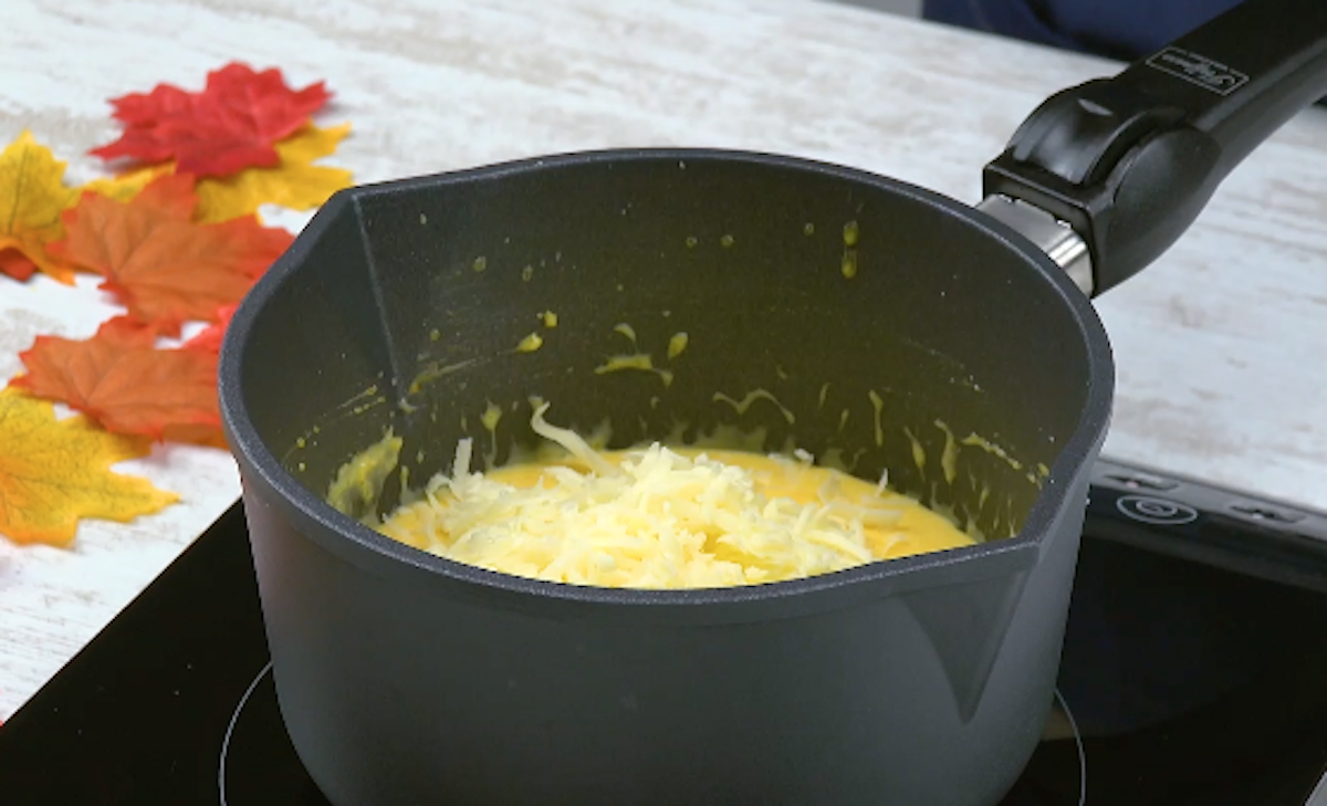 Kürbisfleisch wird mit Milch und geriebenem Käse in Topf erhitzt