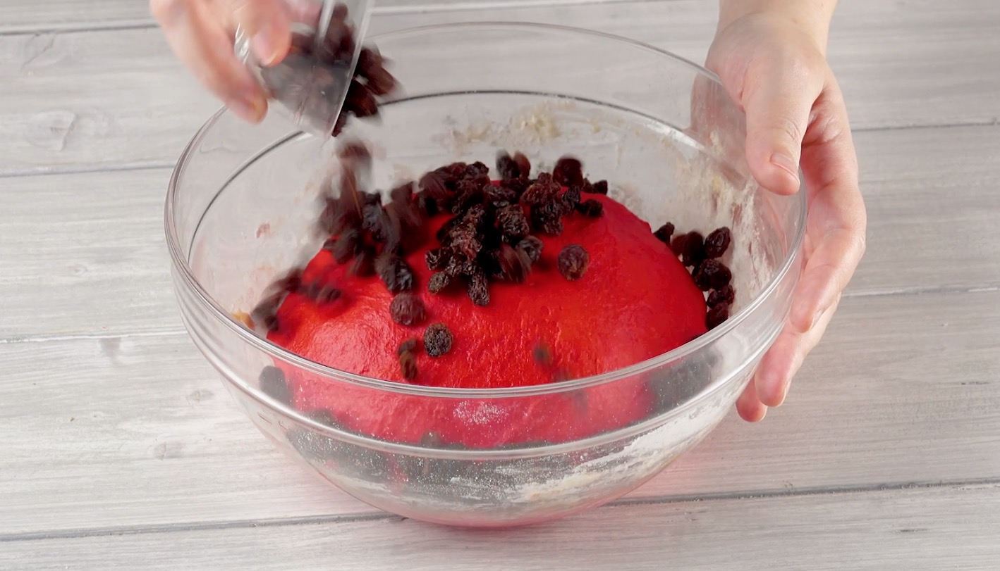 Roter Brotteig in Schüssel wird mit Rosinen versehen