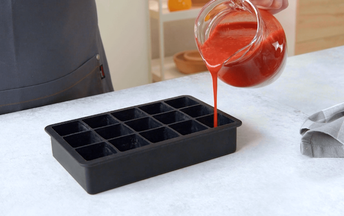 Erdbeerkompott wird in eine Eiswürfelform gegossen.