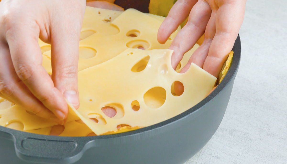 Käsescheiben werden in einer Pfanne abwechselns mit Schinken geschichtet