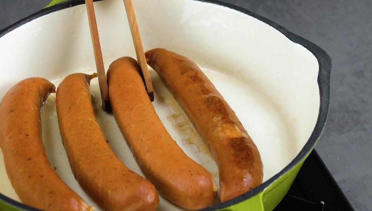 Vier Krakauer Würstchen werden in Pfanne angebraten