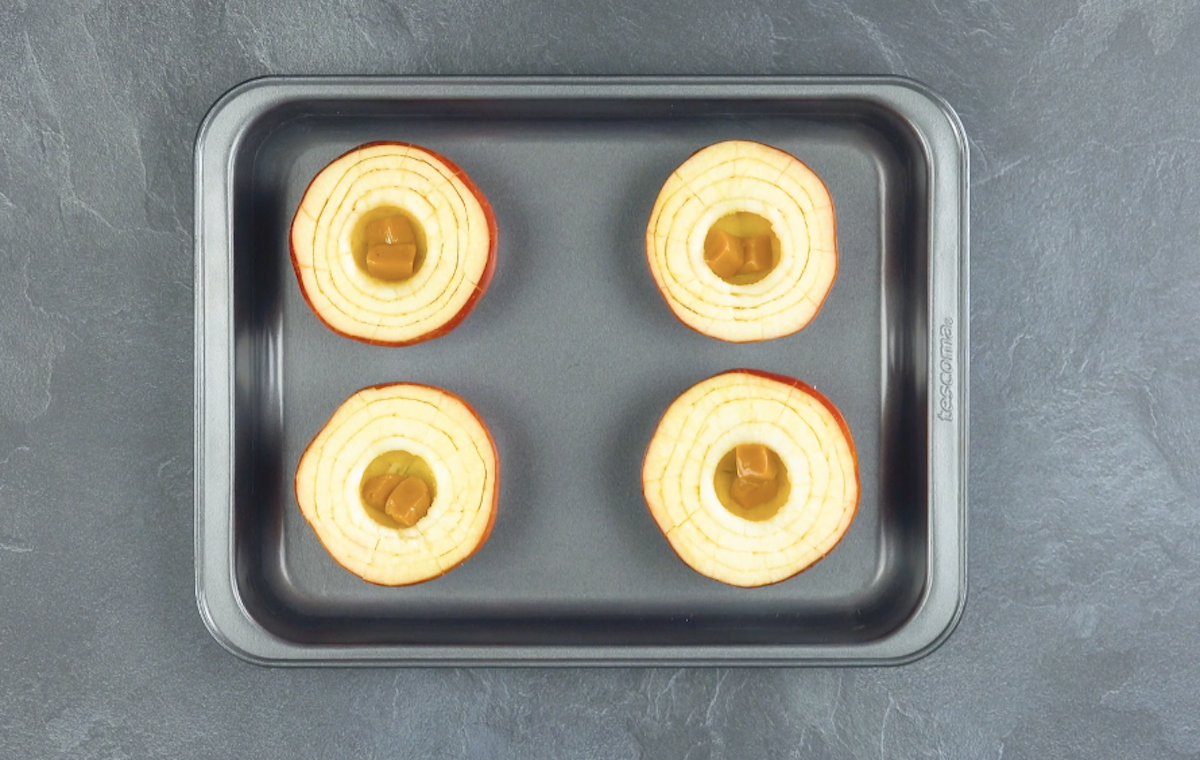 Vier Äpfel auf einem Backblech, die mit je zwei Karamellbonbons gefüllt sind