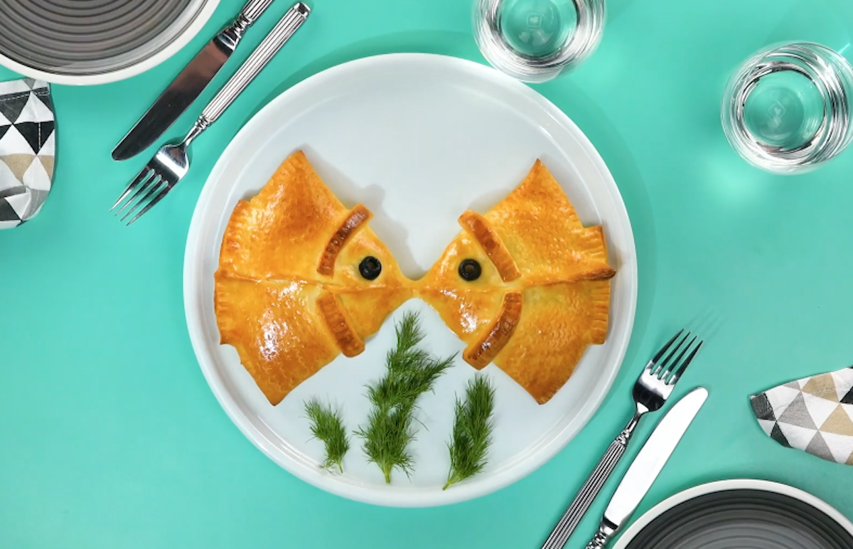 2 Pizzateig-Taschen in Form von Fischen, die sich küssen, auf einem Teller.