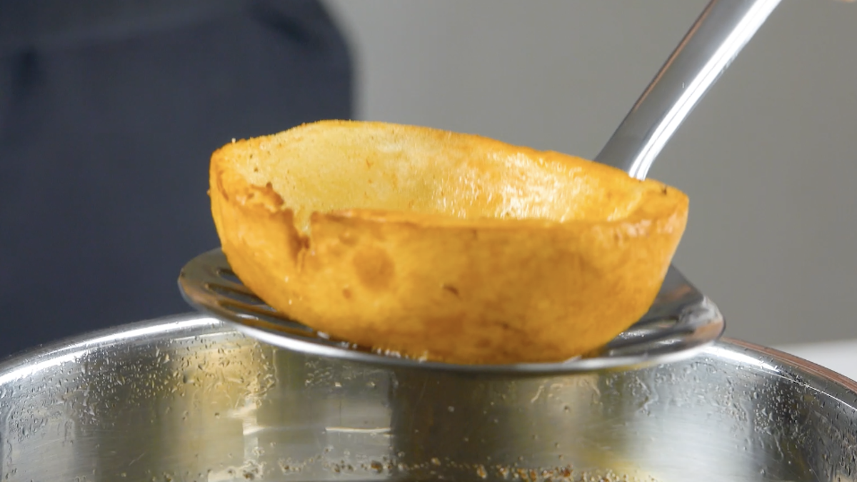 Eine frittierte und ausgehöhlte Kartoffelhälfte auf einem Schaumlöffel