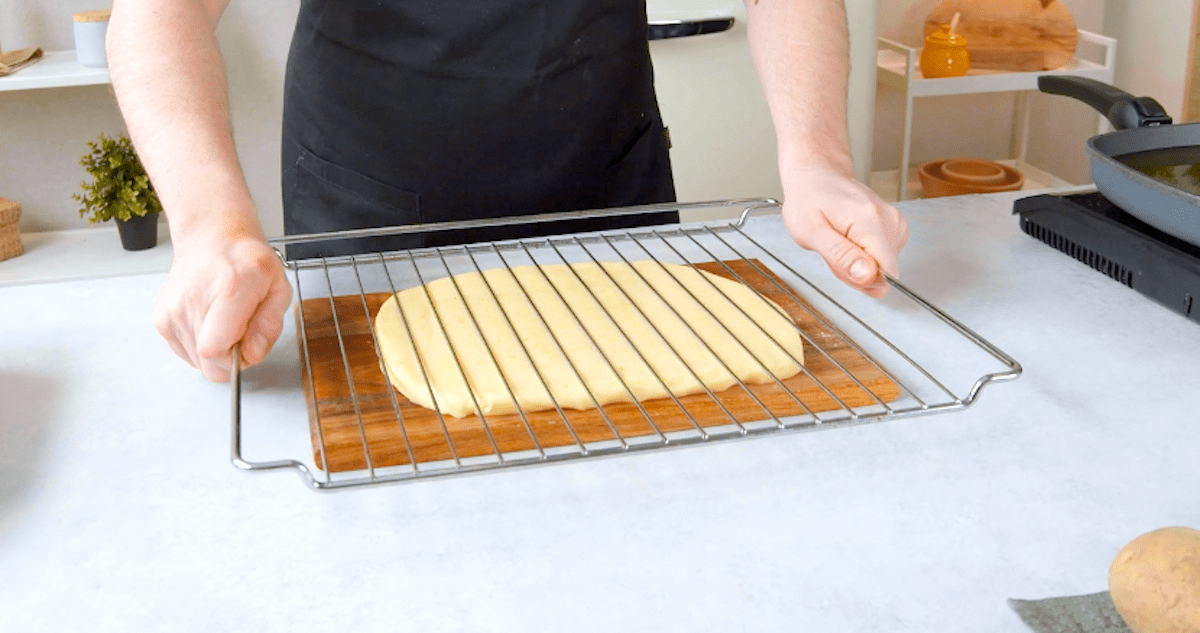 Jemand drückt einen Ofenrost auf eine flach ausgewalzte Schicht Kartoffelbrei.
