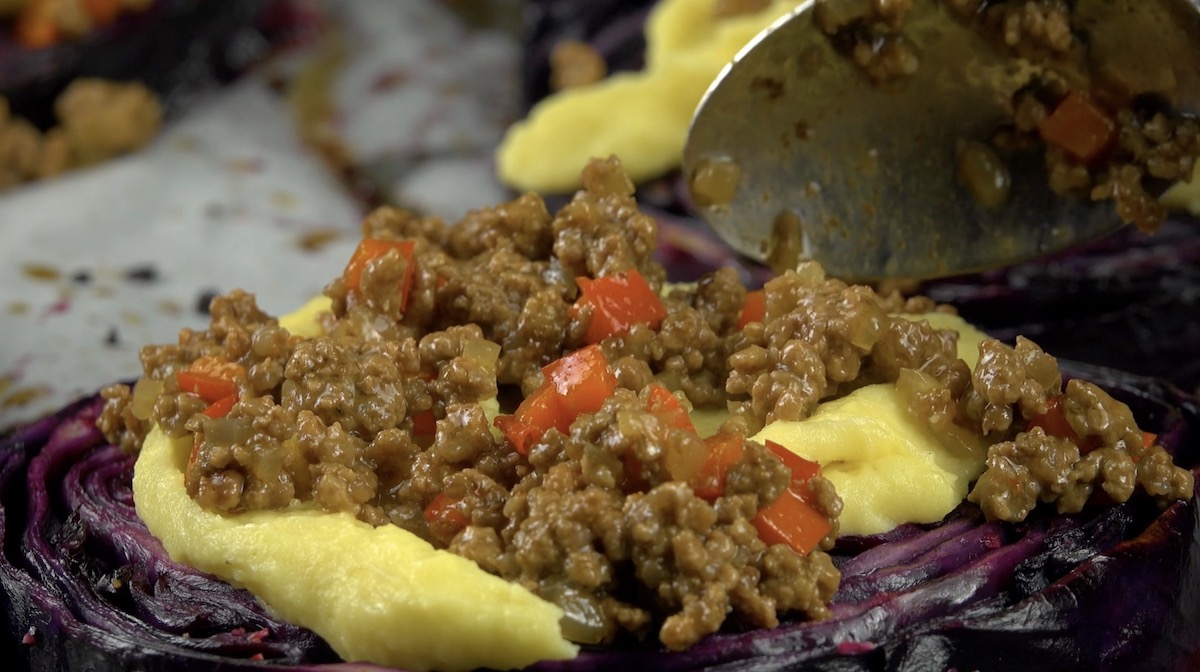 Angebratenes Hackfleisch wird auf Kartoffelpüree auf Rotkohlsteaks verteilt