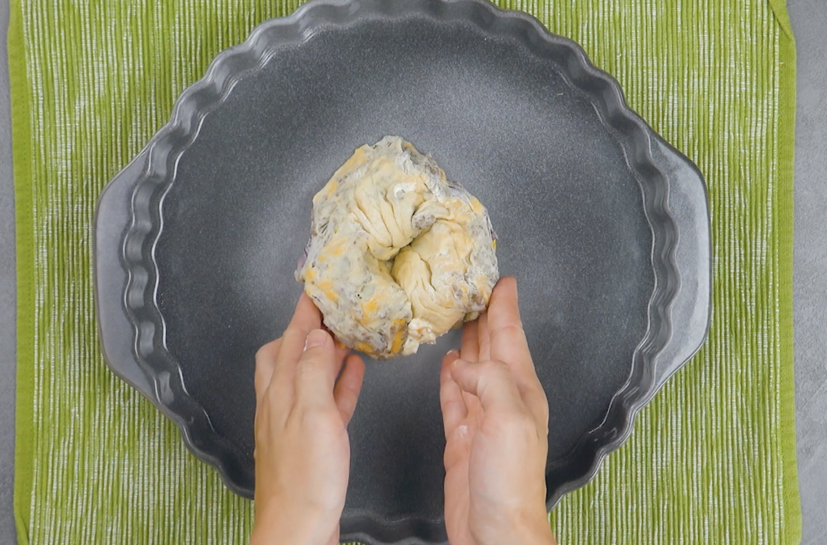 Mit Frischkäse gefüllter Teigschlauch wird kreisförmig mittig in Auflaufform zu Cheeseburger-Kuchen gelegt