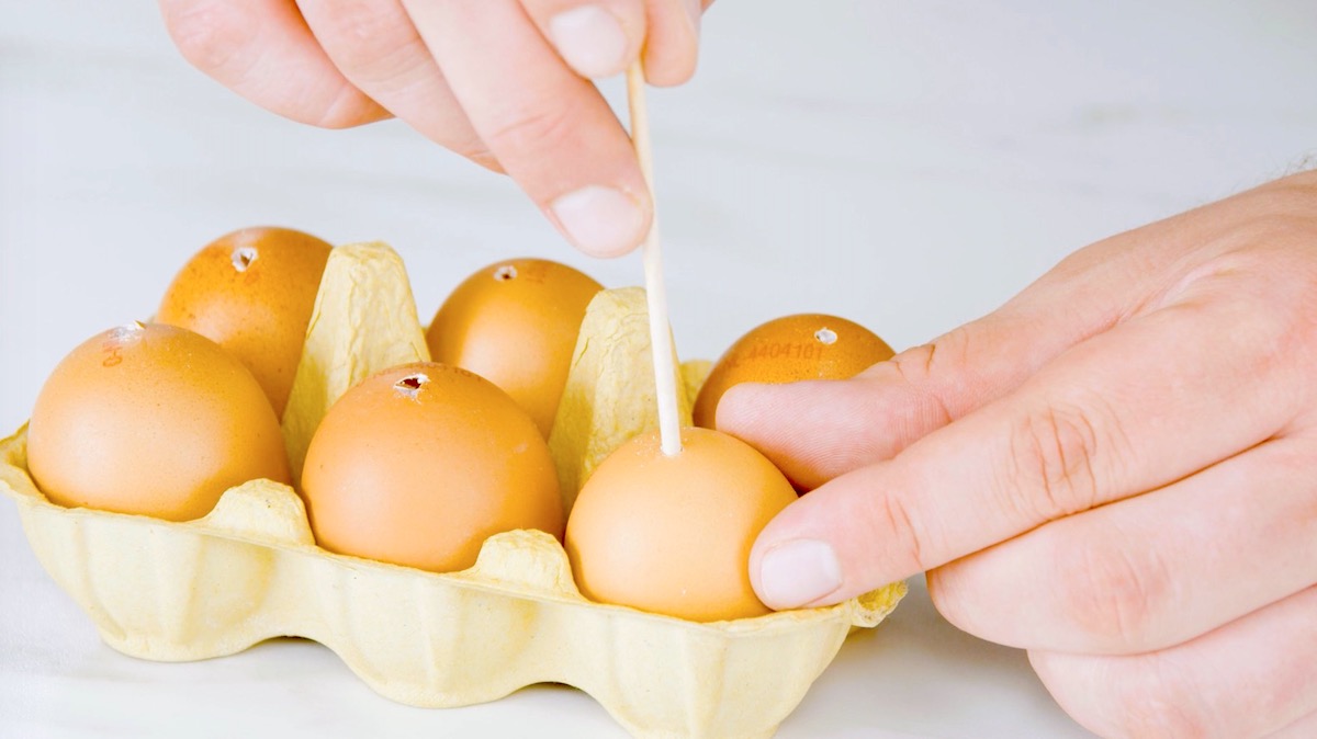 Jemand sticht mit einem Holzstab Löcher in Eier