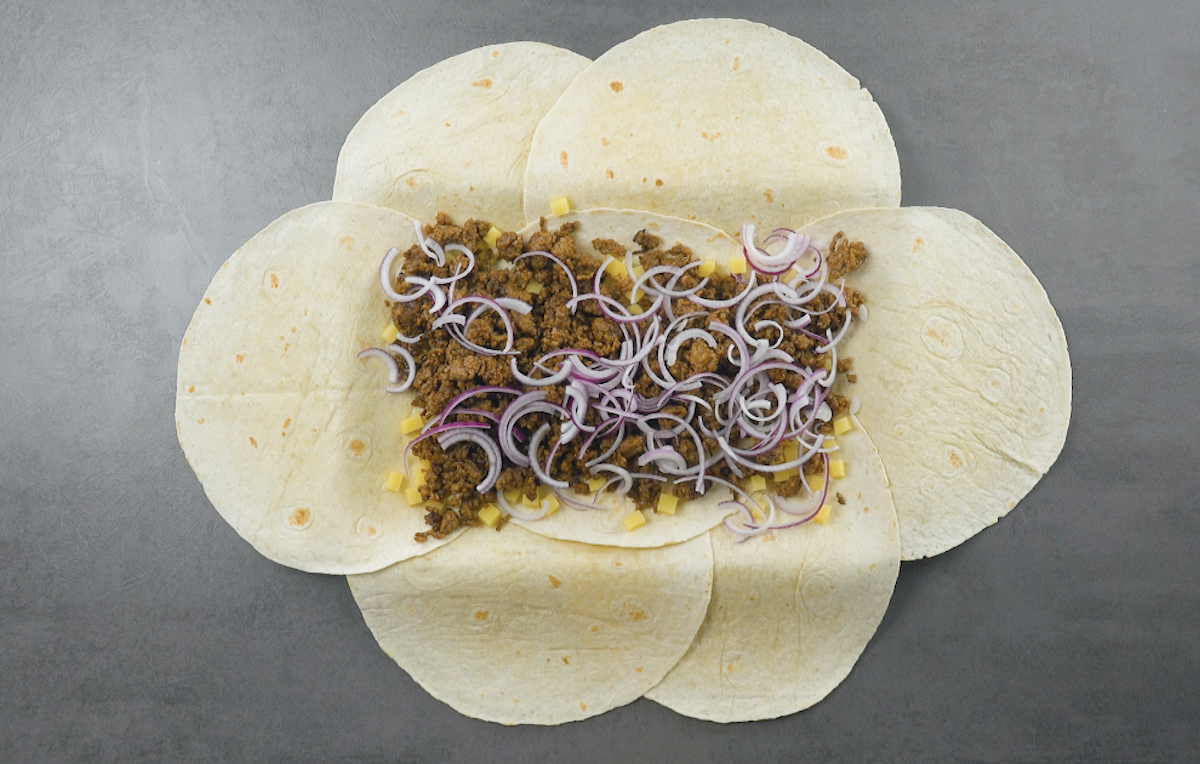 7 Tortillas werden übereinander gelegt und mit Kartoffelwürfeln, gebratenem Hackfleisch und roten Zwiebeln belegt