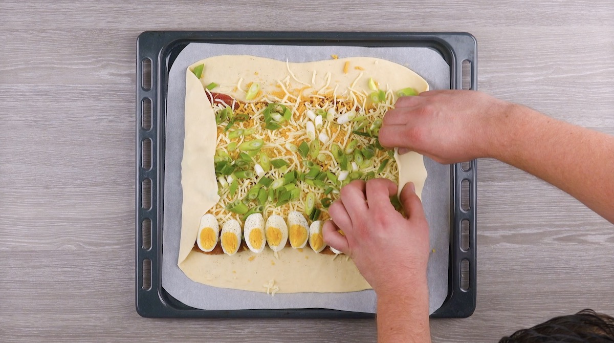 Pizzateig wird um Zutaten für Bauernfrühstück-Calzone gefaltet