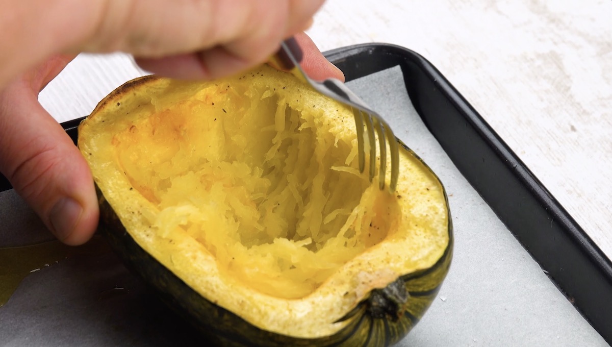 Ein halbierter Spaghettikürbis wird mit einer Gabel ausgehöhlt