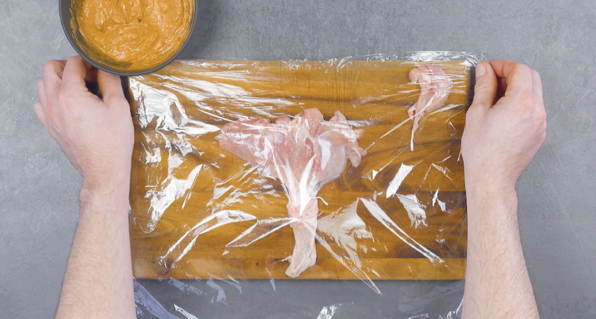Aufgeklapptes Hähnchenfleisch wird mit Frischhaltefolie bedeckt