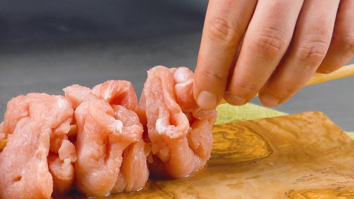 Gefüllte Schweineschnitzel werden nebeneinander auf Holzspieß gespießt