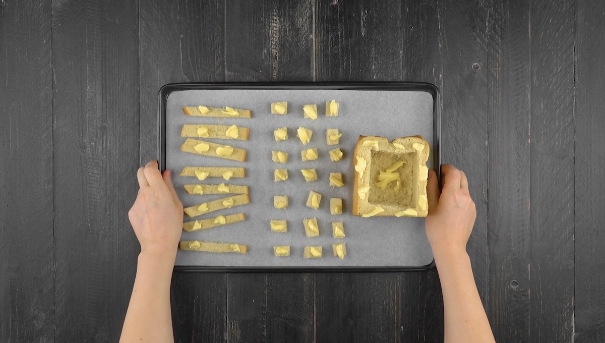 Toast-Quader und Taoststücke werden mit Butter belegt und auf Backblech verteilt