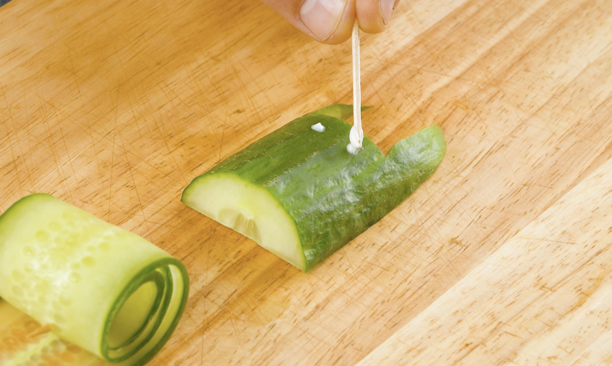 Frischkäse wird als Augen auf Gurke getupft