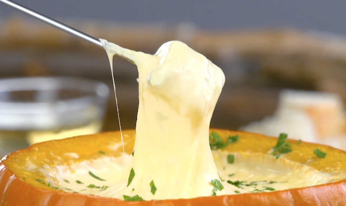 Brotwürfel auf Spieß wird in Käsefondue im Kürbis getaucht