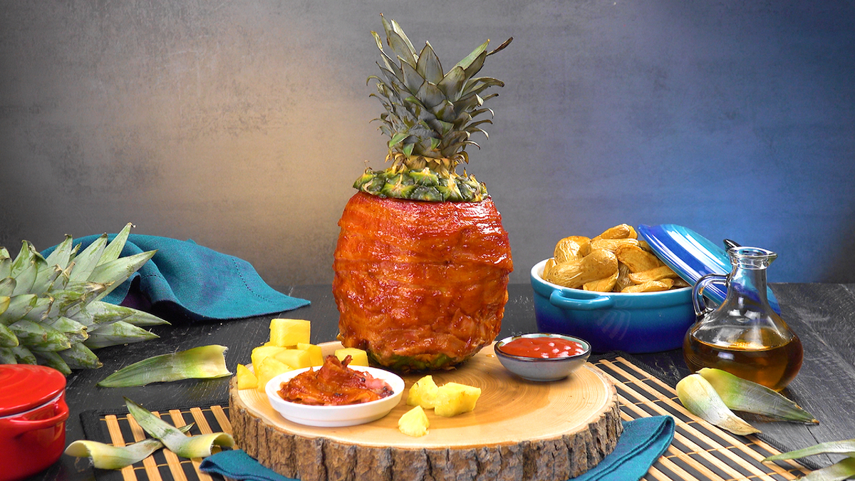 Grillananas, mit Hähnchenbrust gefüllt und mit Bacon umwickelt, neben Beilagen und Dip