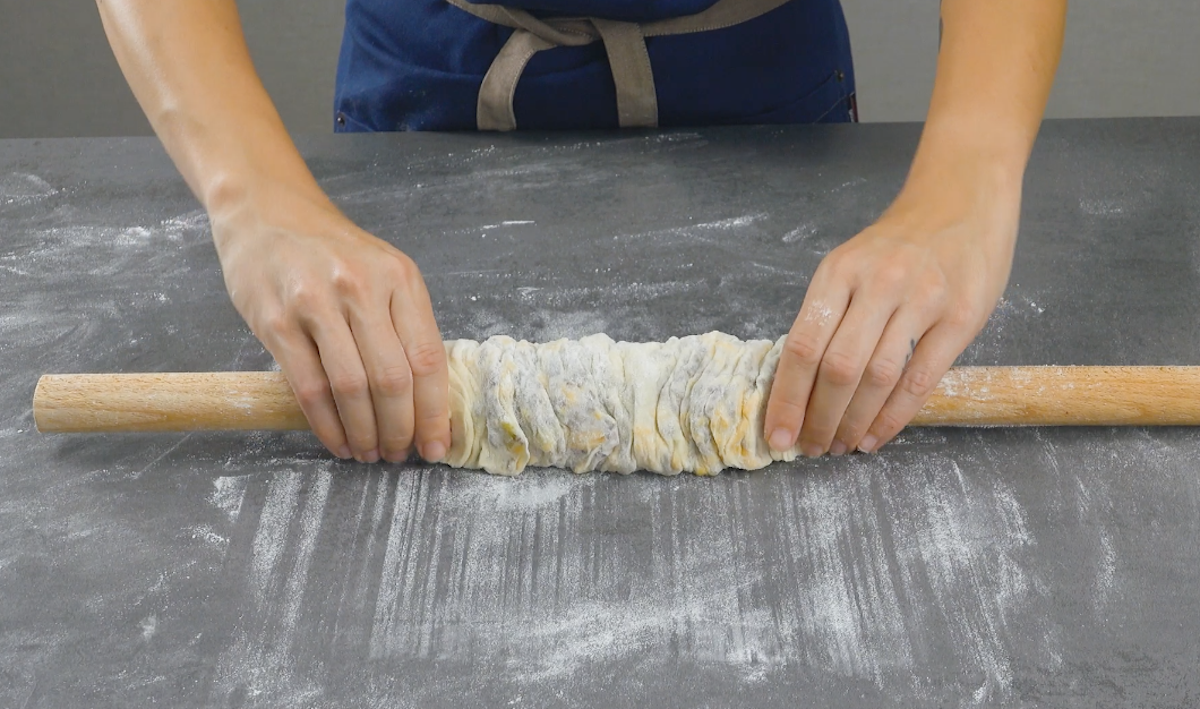 Auf Nudelholz aufgerollter Teig wird mit Händen zur Mitte hin zusammengeschoben
