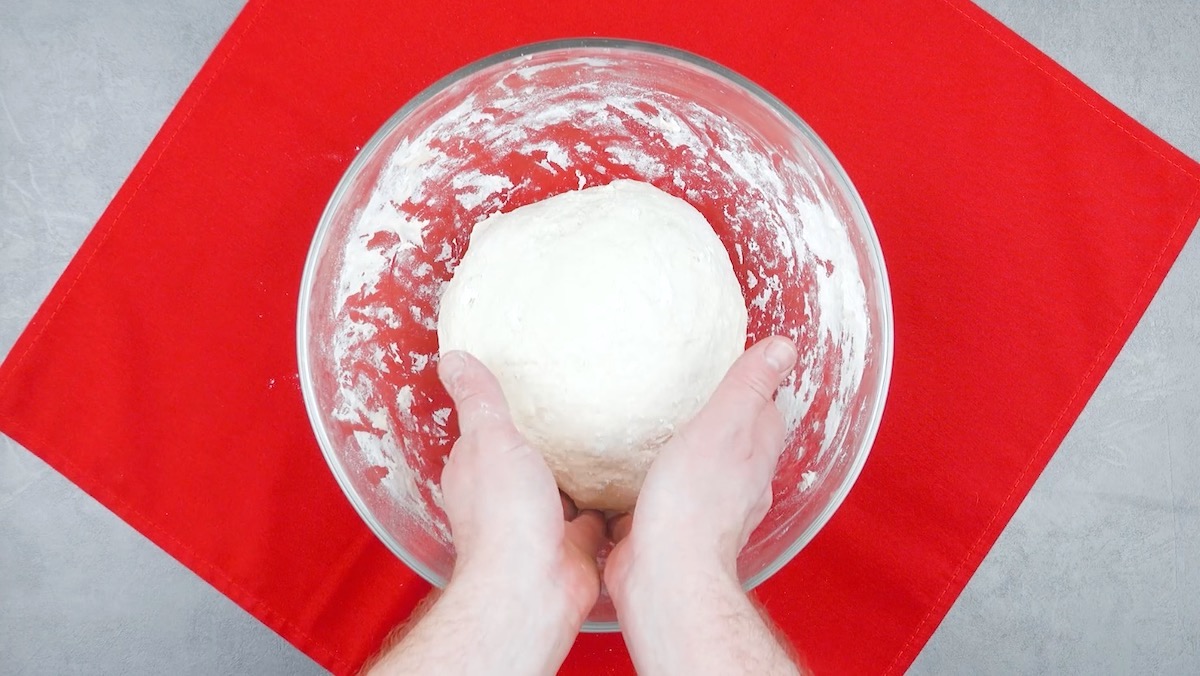 Pizzateig wird in Schüssel mit Händen verknetet