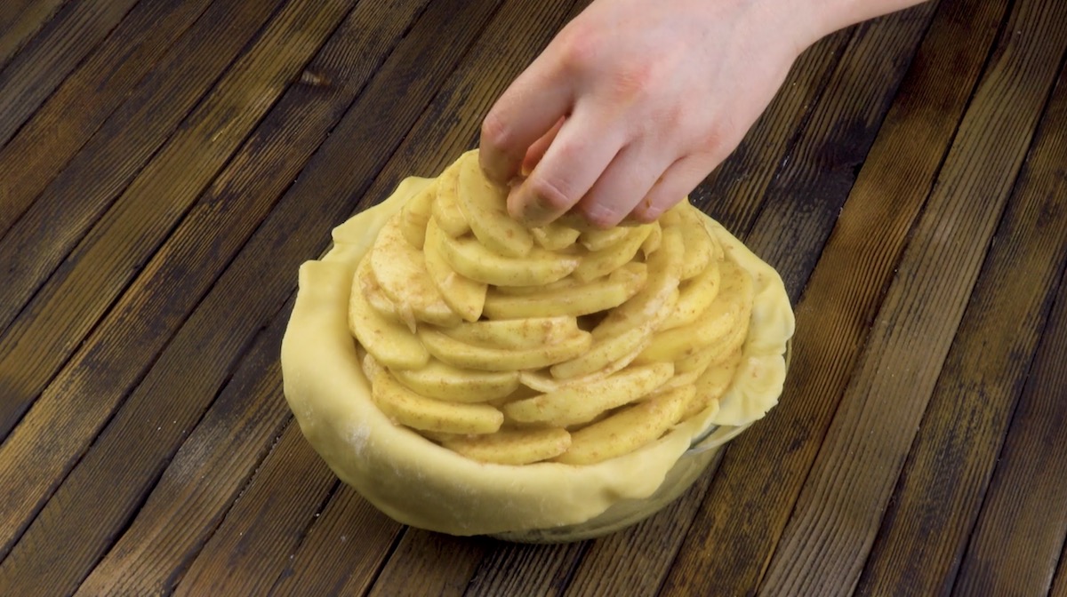 Marinierte Apfelstücke werden aufeinander in eine Kuchenform mit Teig gestapelt