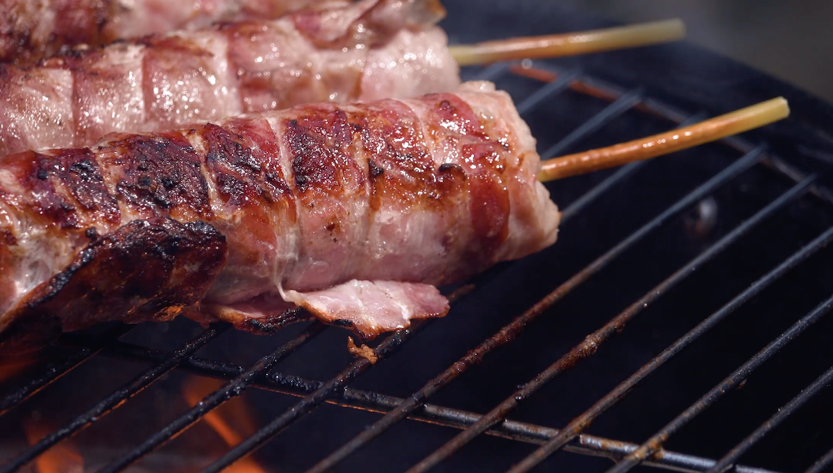 Bratwürste, mit Bacon umwickelt, werden auf Grill geröstet