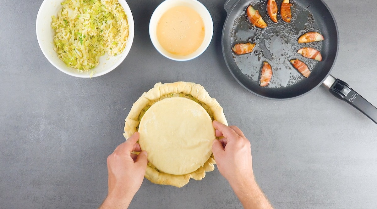 Pizzateig wird auf die Füllung in einer Springform gelegt