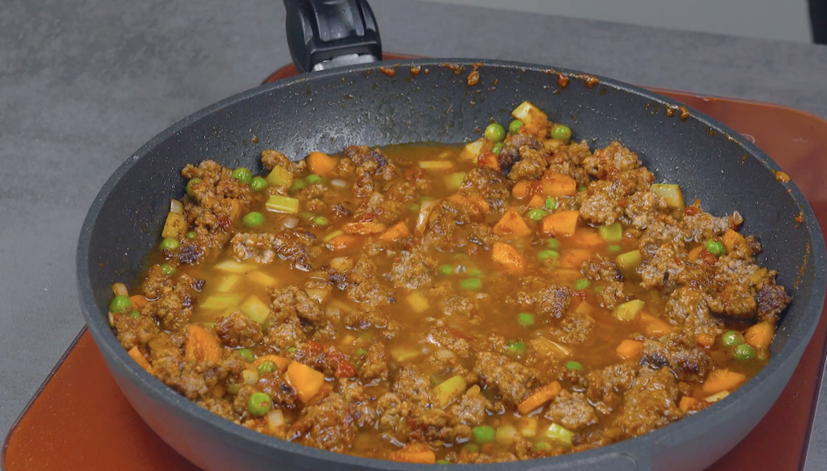 Hackfleisch wird mit Möhren, Sellerie und Erbsen in Pfanne gegart