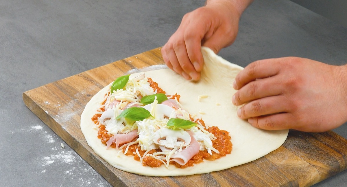 Pizzateig wird zur Hälfte mit Salsiccia und Burrata belegt und zusammengeklappt