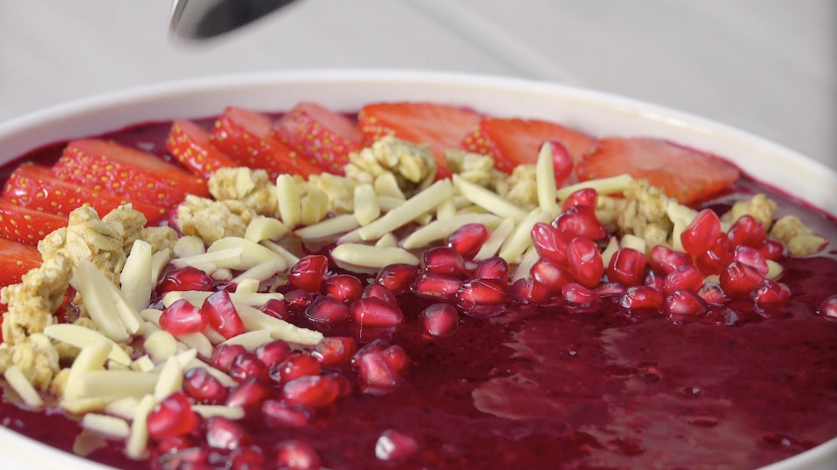 Smoothie-Bowl mit Erdbeeren, Mandelstiften, Granatapfelkernen und Müsli