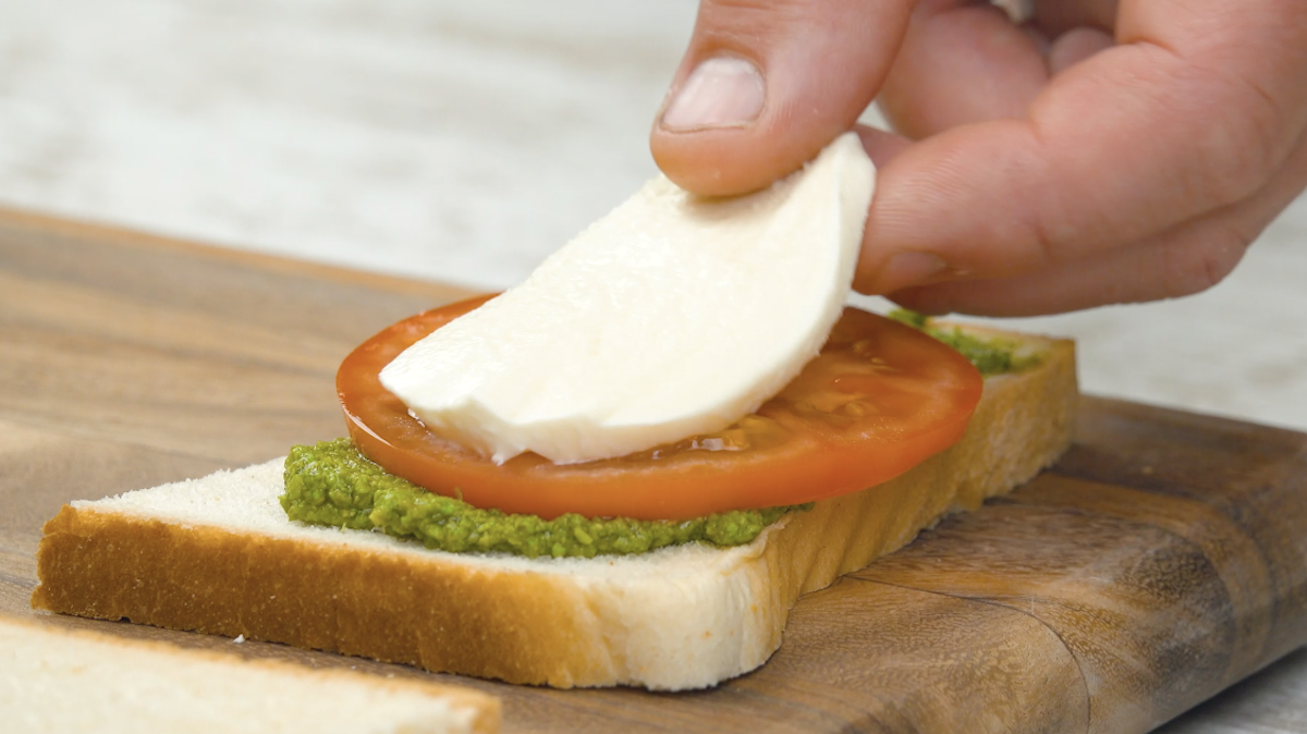 Die größere Toastbrothälfte wird mit Pesto und einer Tomatenscheibe und einer Scheibe Mozzarella belegt