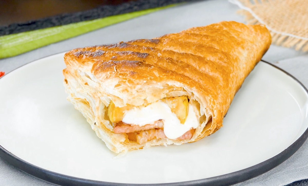 Mit Äpfeln, Käse und Bacon gefüllte Blätterteigtasche, von der abgebissen wurde