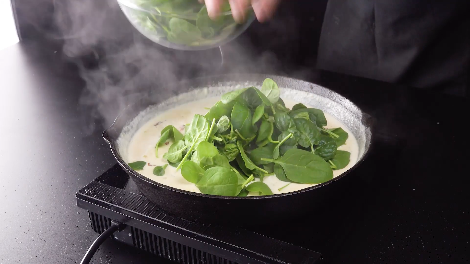 Frischer Spinat wird zu Sahnesoße in Pfanne hinzugegeben