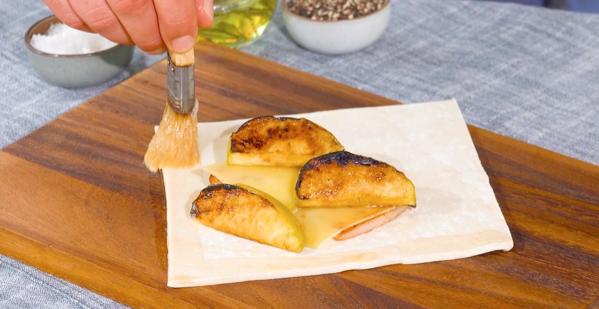 Blätterteig-Quadrat mit Äpfeln, Käse und Bacon wird am Rand mit Ei bepinselt