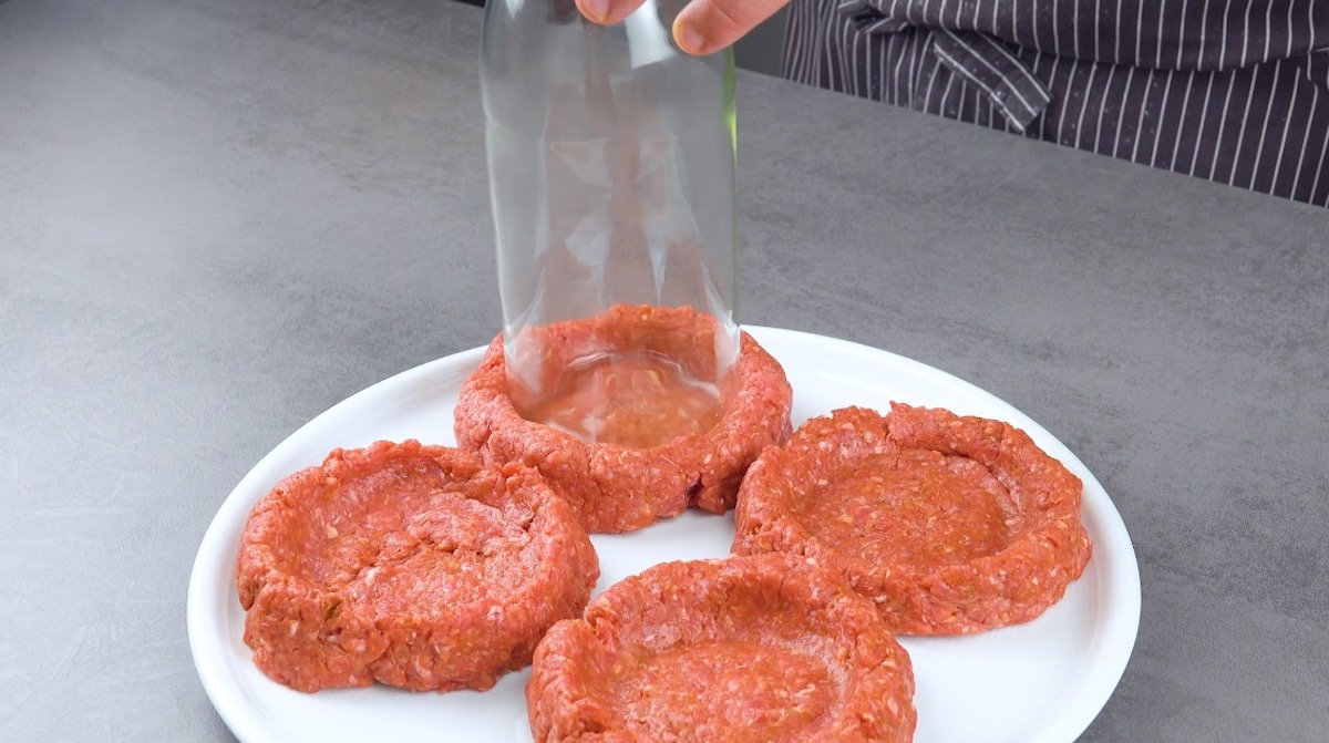 In 4 Burgerpattys aus Hackfleisch wird mit Glasflasche eine Mulde hineingedrückt