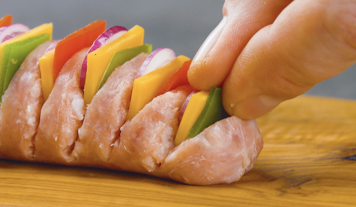 Eingeschnittene Hasselback-Bratwurst wird mit Paprika, Käse und Zwiebel gefüllt