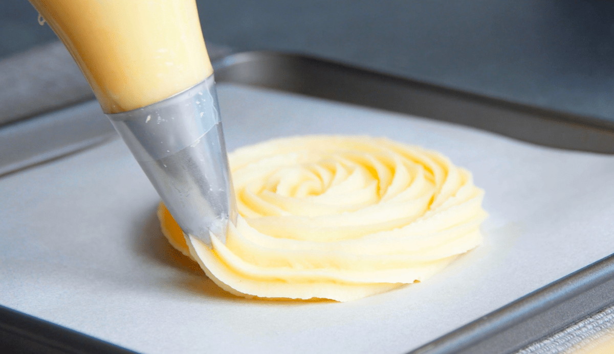 Brandteig wird spiralförmig auf ein Backblech gespritzt