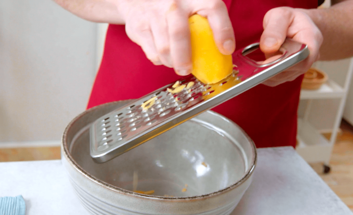 Kartoffeln werden über einer Reibe in eine Schüssel gerieben