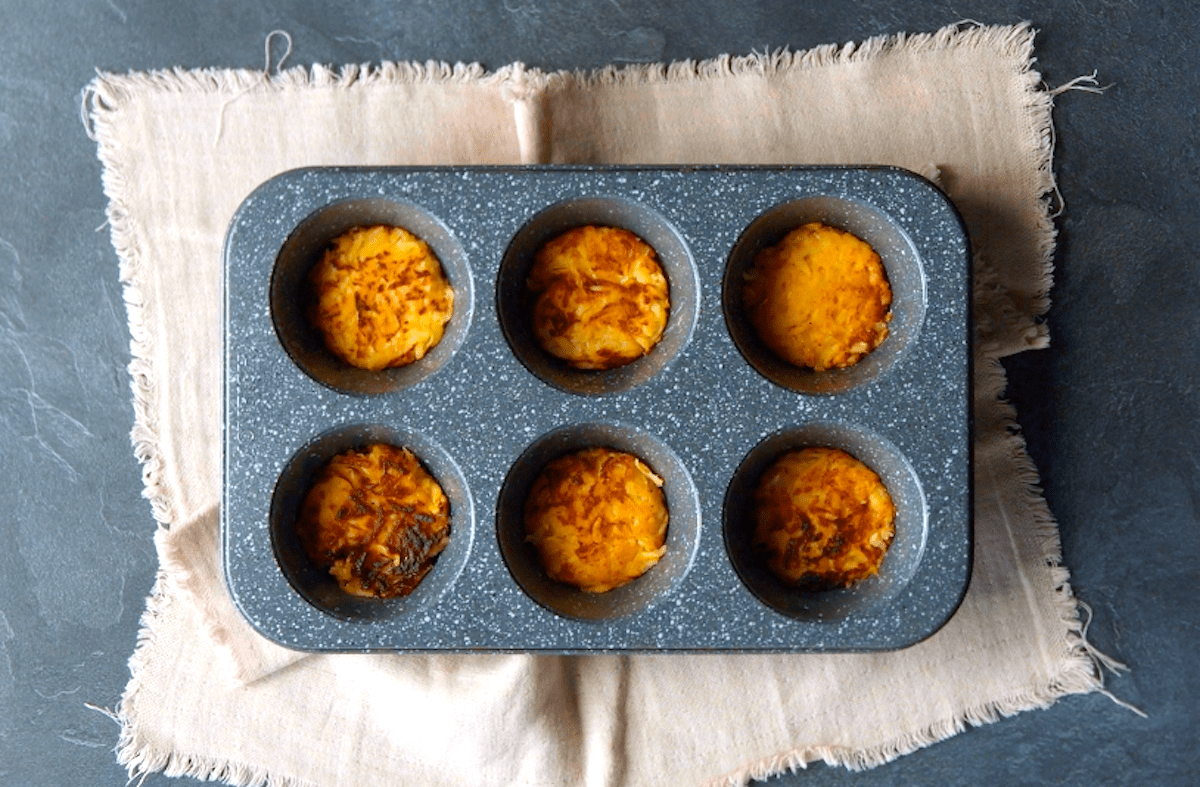 Kartoffelrösti werden in die sechs Mulden einer Muffinform gelegt.
