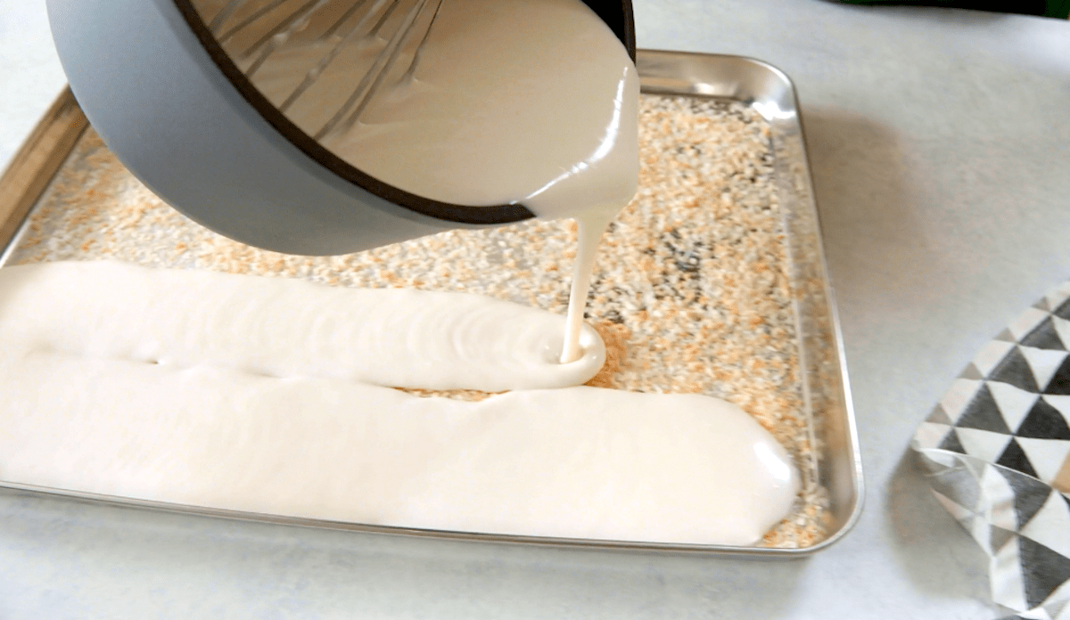 Kokospudding wird auf ein Blech mit gerösteten Kokosraspeln gegossen