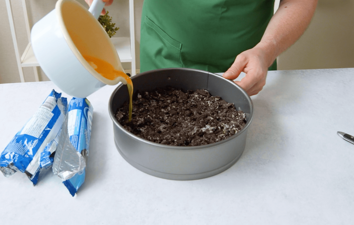 Flüssige Butter wird auf zerstoßene Oreo Kekse in einer Kuchenform gegeben