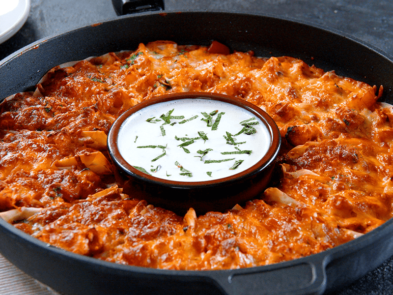 Mit Hähnchen gefüllte Teigtaschen in einer Form, ein Schälchen mit Dip steht in der Mitte.