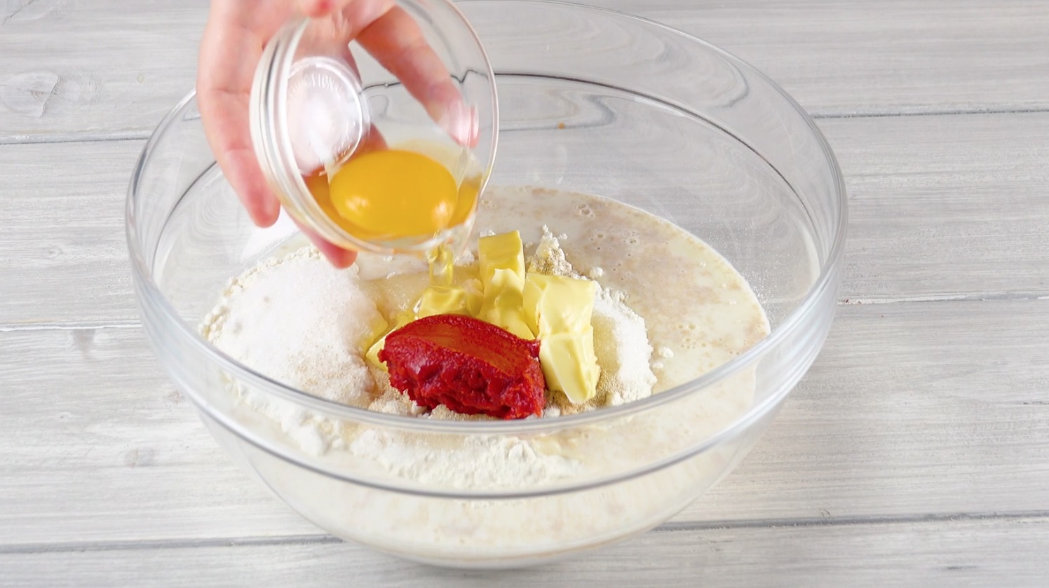 Ei wird zu Zutaten für Brotteig in Schüssel hinzugefügt