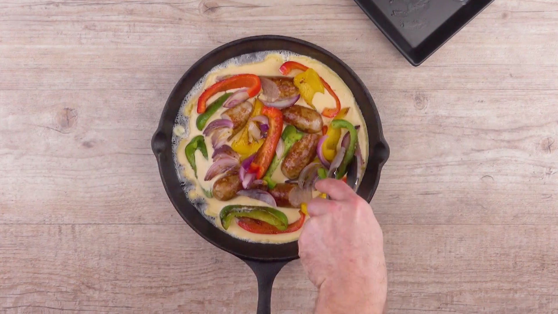 Paprikasteifen und Bratwürste werden in Pfannkuchenteig in einer Pfanne gegeben