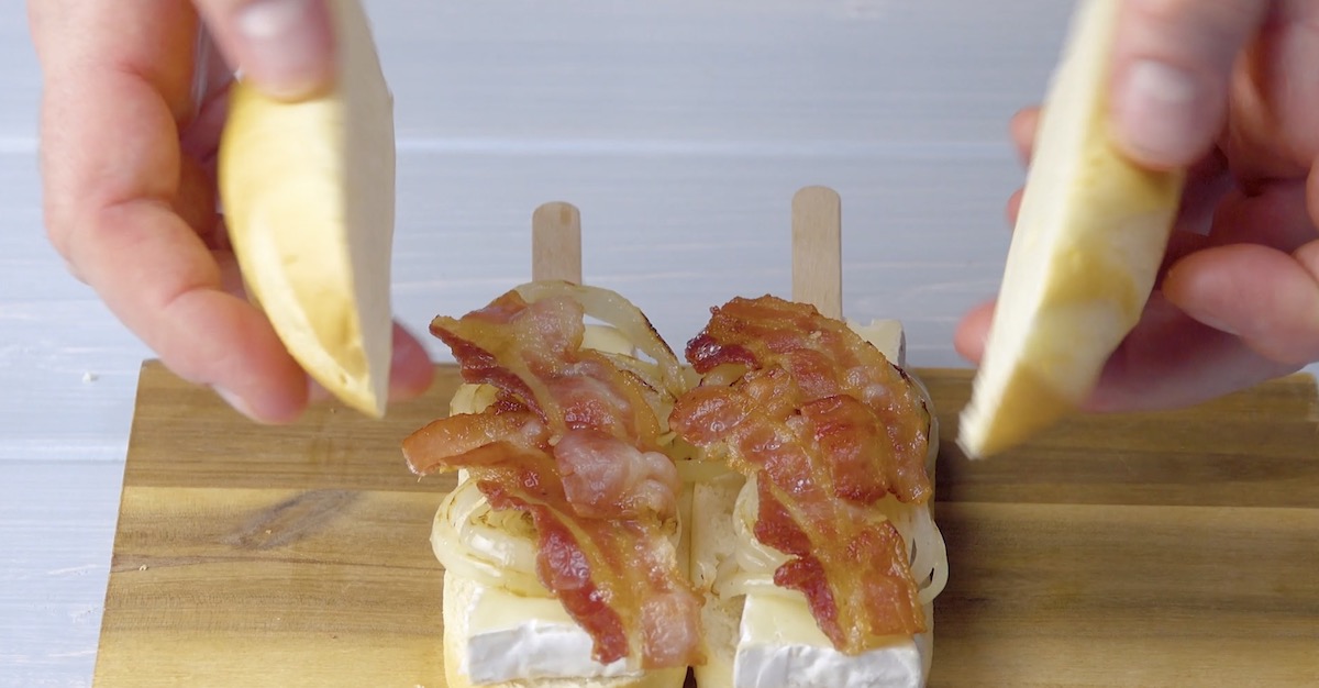 Gebratene Zwiebeln und Bacon werden auf belegte Milchbrötchenhälften gelegt.